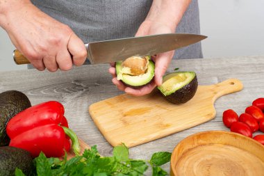 Avokado hazırlayan aşçı kadın. Mutfak masasında çeşitli sebze ve baharatlar var..