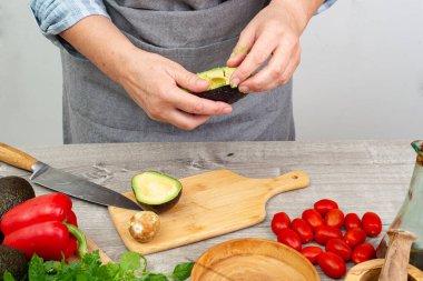 Avokadoyu servis için hazırla. Mutfak masasında çeşitli sebze ve baharatlar var. Kapat..