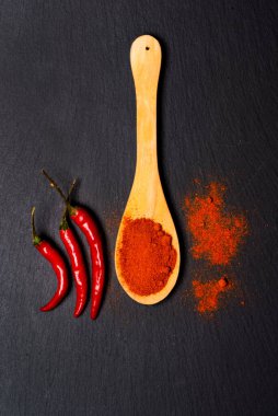 Ahşap kaşıkta kırmızı biber ve siyah taş zemin üzerinde taze biber kabukları. en üstteki görünüm.