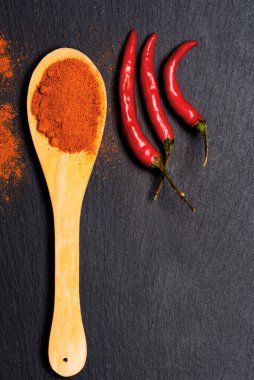 Ahşap kaşıkta kırmızı biber ve siyah taş zemin üzerinde taze biber kabukları. en üstteki görünüm.