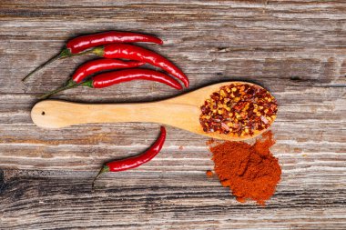 Ahşap arka planda taze biber kabukları olan ahşap bir kaşıkta öğütülmüş kırmızı biber. en üstteki görünüm.