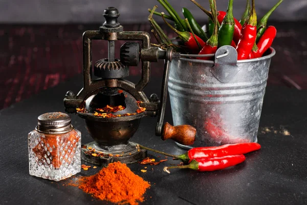 pepper mill, bunch of red peppers, capsicum and pepper pot on a black table. Close-up. Selective focus. Space for text.