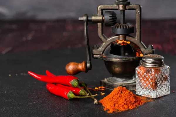 pepper mill, a bunch of red peppers, capsicum and pepper pot on a black table. Close-up. Selective focus. Space for text.