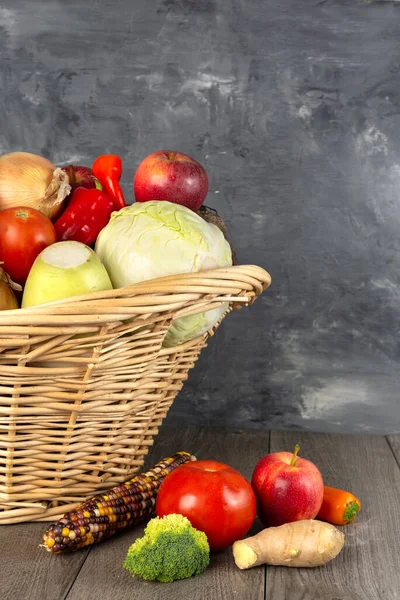 wicker basket with vegetables and fruits against a gray wall. Space for text.