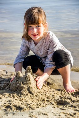 Küçük bir kız nehir sahilinde kedi heykeli yapıyor.