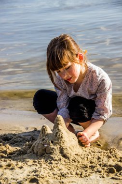 Küçük bir kız nehir sahilinde kedi heykeli yapıyor.