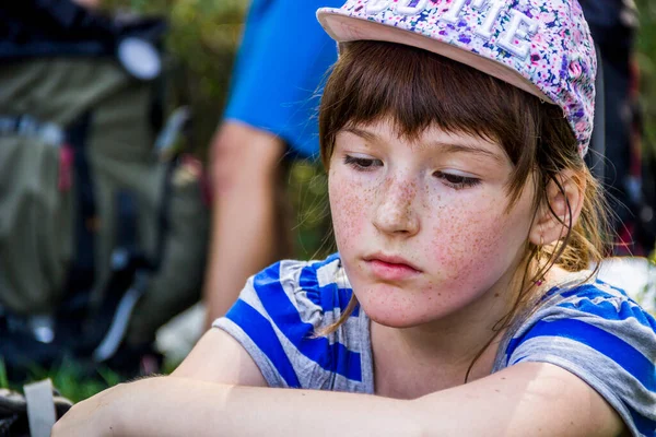 close-up portrait of a girl sitting on grass near the rucksack