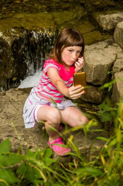 Ormandaki küçük şelalenin yanında küçük bir kızın selfie çekerken.