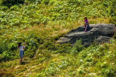 Ormandaki büyük taşın üstünde küçük kız kardeşinin fotoğrafını çeken genç bir kız.