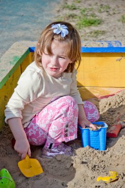 Kum havuzunda kumla oynayan sevimli küçük bir kız.