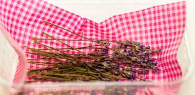 sprigs with dried lavender flowers in a plastic box on a piece of red checkered cloth