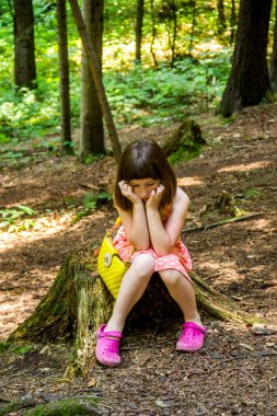 a sad little girl sit on the stamp in the forest