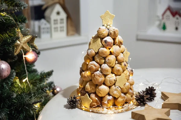 Croquembouche profiterollü pasta karamel ve vanilyalı krema arkaplanda yılbaşı ağacı ile birlikte.