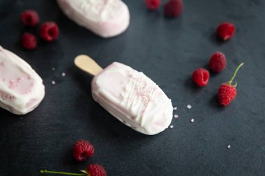 Ahudududulu cheesecake veya kremalı tatlı üzerine pembe şeker serpiştirilmiş buzlu dondurma, üzerinde beyaz çikolata ve taze ahududu.