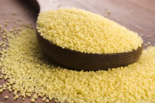 Couscous in wooden spoon on kitchen table — Stock Photo, Image