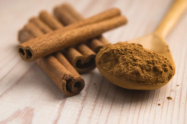 Cinnamon, whole sticks behind wooden spoon with a heap of powder — Stock Photo, Image