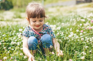 Güler yüzlü küçük kız yonca tarlasında oturuyor, yazın tadını çıkarıyor.