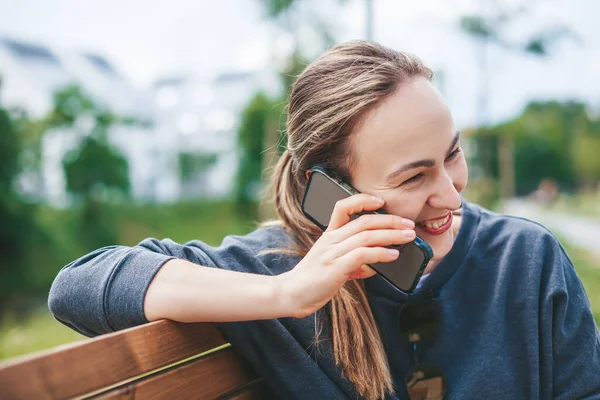 Mujer Joven Cándida Sonriendo Mientras Habla Por Teléfono Sentada Banco —  Fotos de Stock