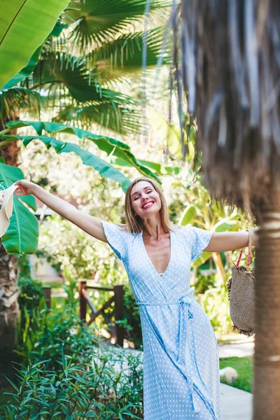 穿着蓝色长裙的年轻漂亮的女人在一个绿色的热带花园里感到快乐和自由 — 图库照片