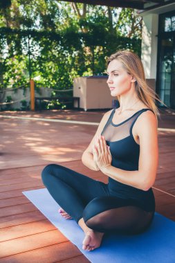 Tropik bir tatil köyünde yoga yaparken lotus pozisyonunda oturan güzel, rahatlatıcı bir kadın.
