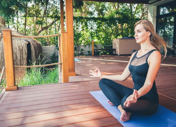 Tropik bir tatil köyünde yoga yaparken lotus pozisyonunda oturan güzel, rahatlatıcı bir kadın.