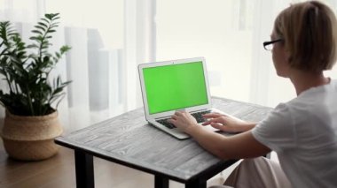 Evde çalışan bir kadın, yeşil ekranlı bir laptop kullanıyor.