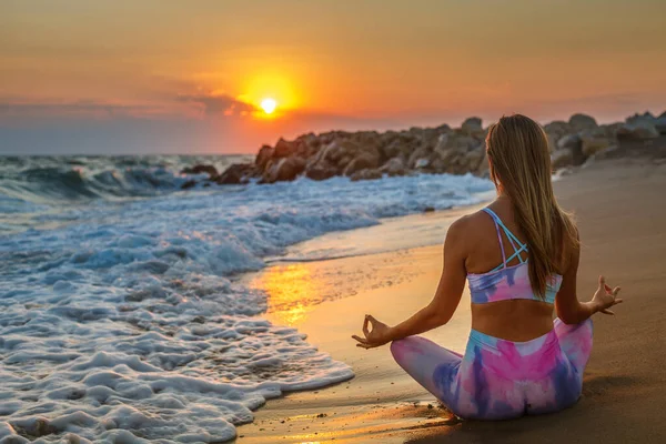 日落时 在海滩上练习瑜伽的女人的后背以莲花的姿势坐着 她在看太阳 内心和谐与自理 — 图库照片