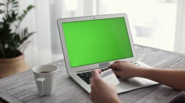 Çevrimiçi alışveriş yapan bir kadın yeşil ekran ve kredi kartı kullanan bir laptop kullanıyor.