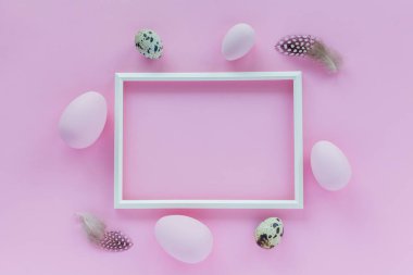 Renkli pastel yumurtalar, bıldırcın yumurtaları, fotoğraf çerçevesi ve pembe arka planda tüyleri olan minimalist Paskalya bayramı arkaplanı. Metin için yeri olan düz bir tebrik kartı. Paskalya dekorasyonu, minimalist tasarım, modern tasarım şablonu.