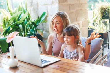 Sarışın kadın ve tatlı küçük kızı laptoplarını kullanarak arkadaşlarıyla ya da akrabalarıyla görüntülü sohbet ediyorlar.