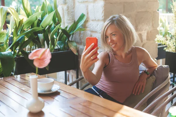 Блондинка Усміхнена Жінка Робить Селфі Червоному Телефоні Сидячи Затишному Кафе — стокове фото