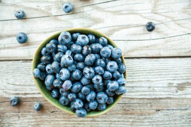 Gri ahşap arka planda bir kasede taze olgun yaban mersini.