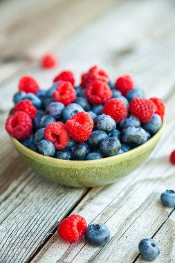 Yakın plan olgun yaban mersini ve ahududu ahşap arka planda bir kasede.