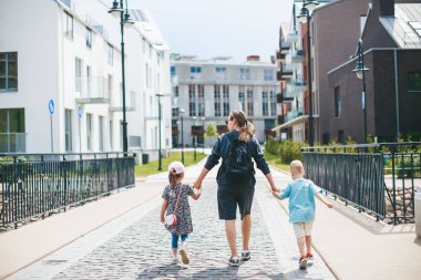 Anne ve iki çocuğu - bir oğlan ve bir kız, kasabada el ele yürüyorlar.