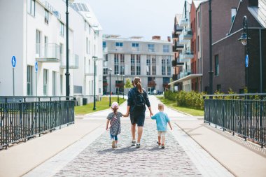 Anne ve iki çocuğu - bir oğlan ve bir kız, sabah anaokuluna giderken el ele tutuşuyorlar.