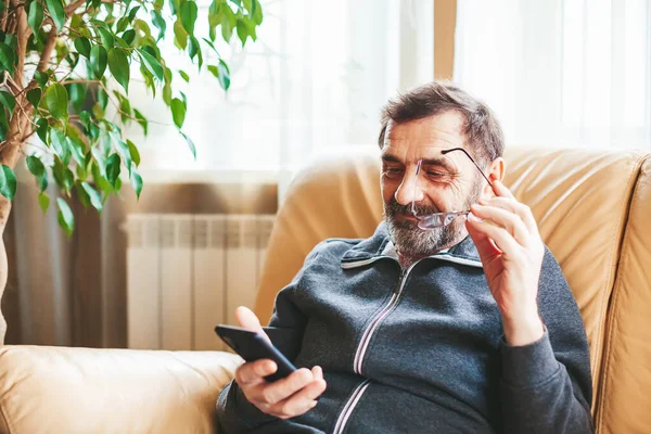 안경을 소파에 검색하거나 스마트폰으로 뉴스를 개념을 사용하는 노인들 스톡 이미지