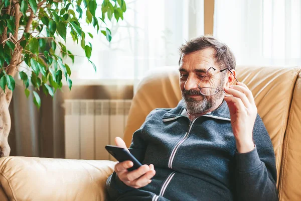 Hombre Maduro Con Gafas Sentado Sofá Buscando Leyendo Algo Smartphone —  Fotos de Stock