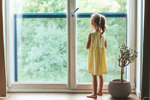 Mała Dziewczynka Żółtej Sukience Stojąca Przy Oknie Patrząca Przez Nie — Zdjęcie stockowe