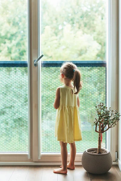 Вид Ззаду Маленької Дівчинки Жовтій Сукні Стоїть Біля Вікна Дивиться — стокове фото