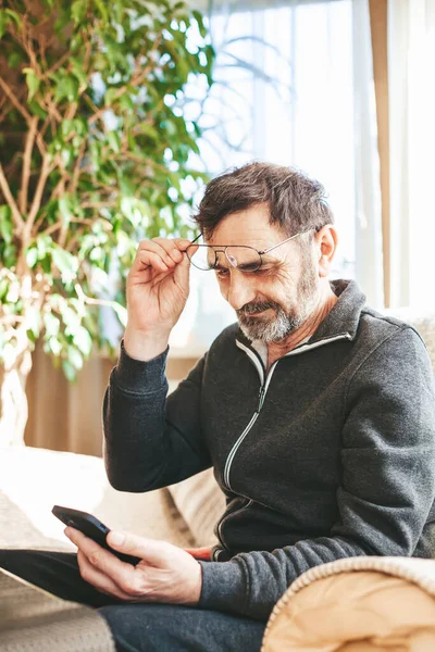 Hombre Maduro Años Con Gafas Vista Sentado Sofá Leyendo Smartphone —  Fotos de Stock