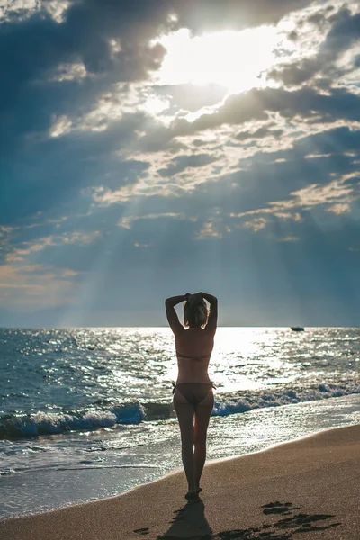 Rear view of a woman in swimwear walking along the beach. She\'s watching the sun.