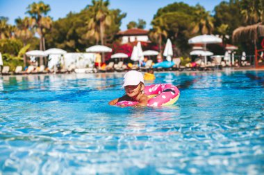 Yüzen yüzüklü şirin küçük kız tropik bir tatil köyünde havuzda yüzüyor.