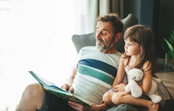 爷爷坐在豆袋椅子上 给孙女读一本书 — 图库照片
