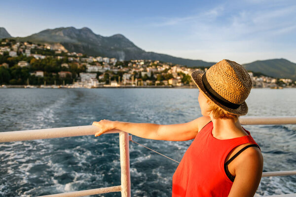 Загорелая женщина в соломенной шляпе сзади смотрит на город Херцег-Нови с лодки - Которский залив, Черногория
