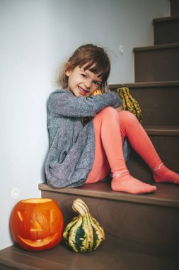 Cadılar Bayramı balkabağı süslemesiyle merdivenlerde oturan sevimli, küçük kız.