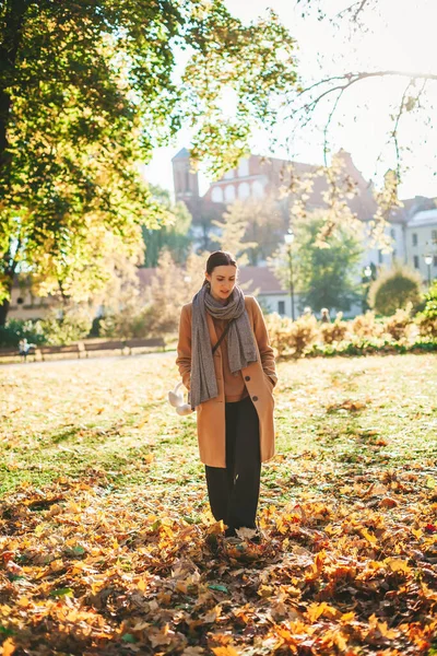 晴れた日に美しい秋の公園を歩くベージュのコートの若い女性 — ストック写真