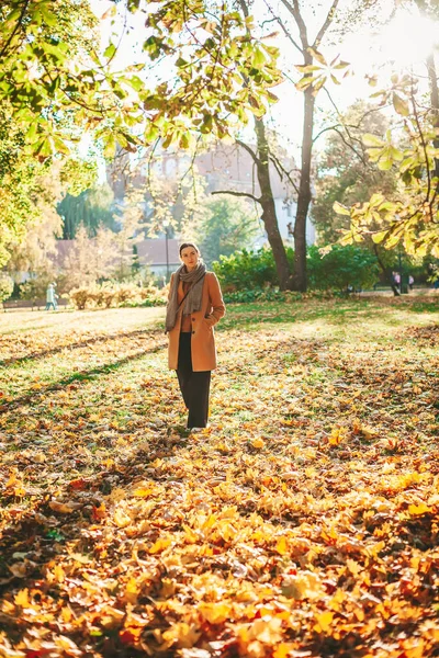美しい秋の公園で晴れた日に黄色の葉の上を歩くベージュのコートの女性 — ストック写真