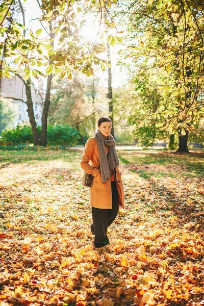 晴れた日に美しい秋の公園を歩くベージュのコートの若い女性 — ストック写真