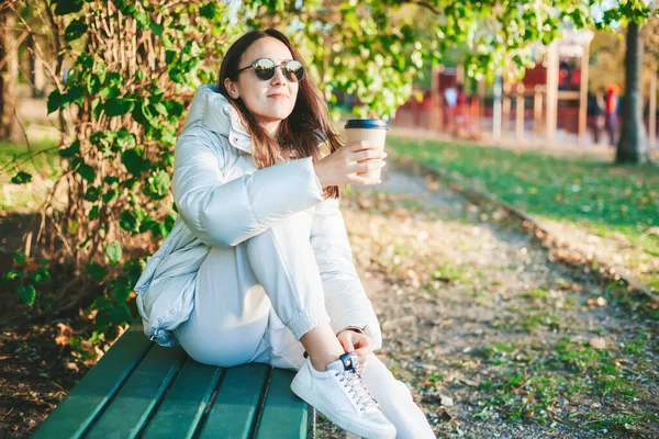 Güneş Gözlüklü Bir Kadın Tek Kullanımlık Kahve Bardağıyla Bankta Oturuyor — Stok fotoğraf