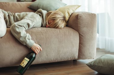 Kanepede uyuyan sarhoş bir kadın, elinde bir şişe viskiyle. Alkolik, sosyal sorun, stres, bağımlılık ve yalnızlık kavramı.
